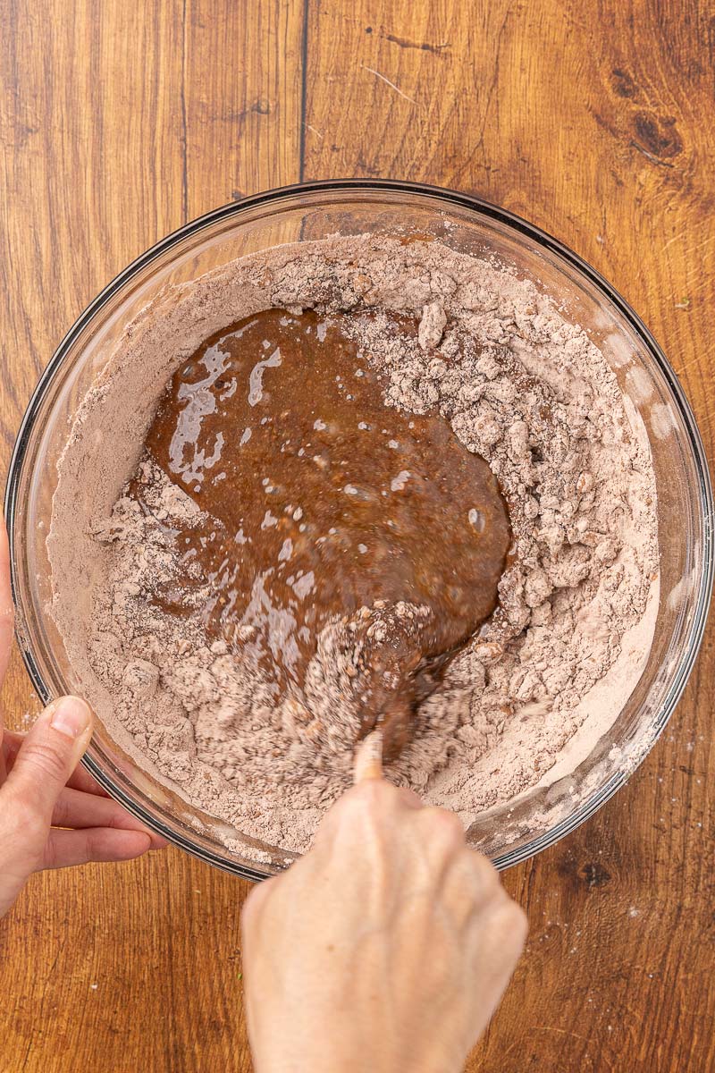 Hands folding wet and dry muffin ingredients together in a bowl.