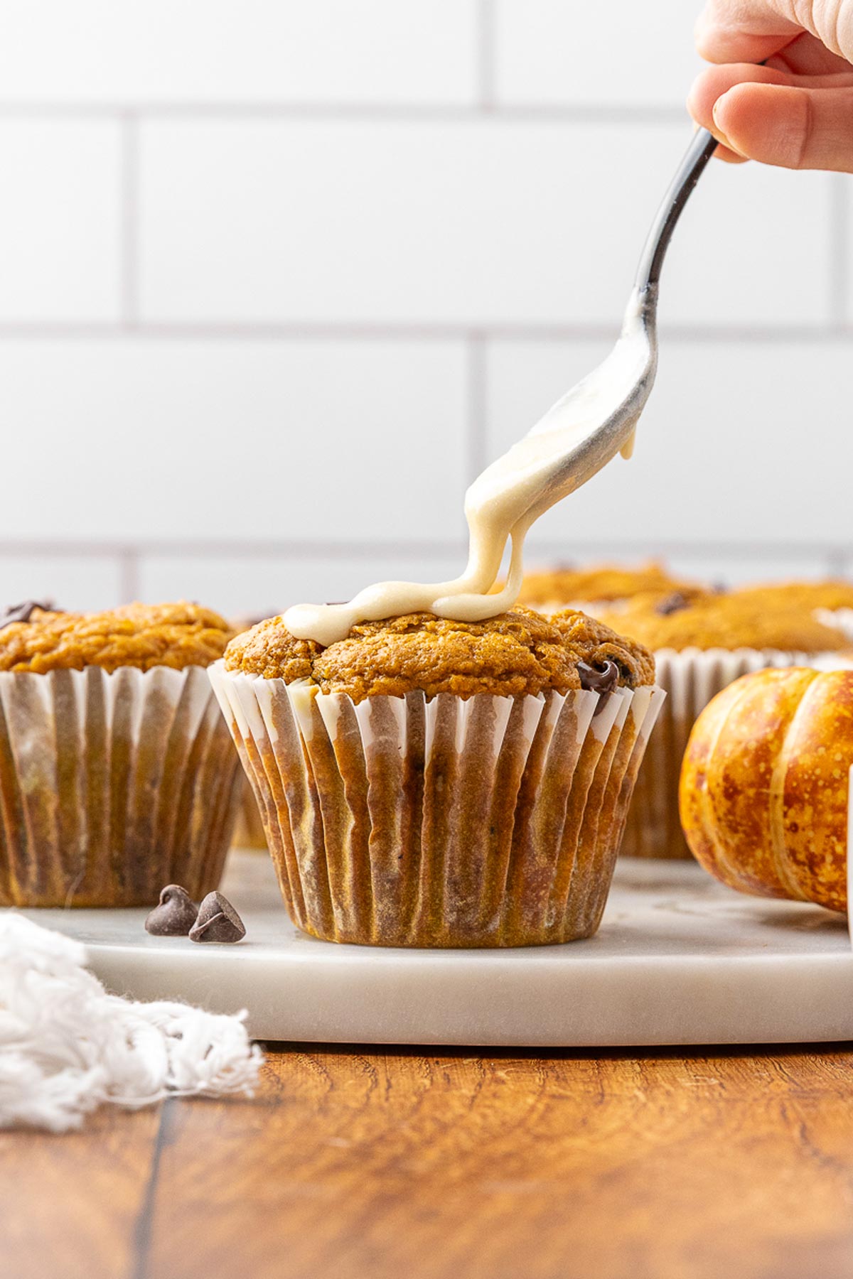 A spoon drizzling maple icing over a pumpkin chocolate chip muffin.