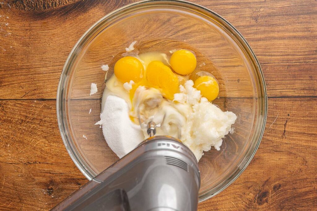 An electric mixer whisking eggs, coconut oil, and sugar.