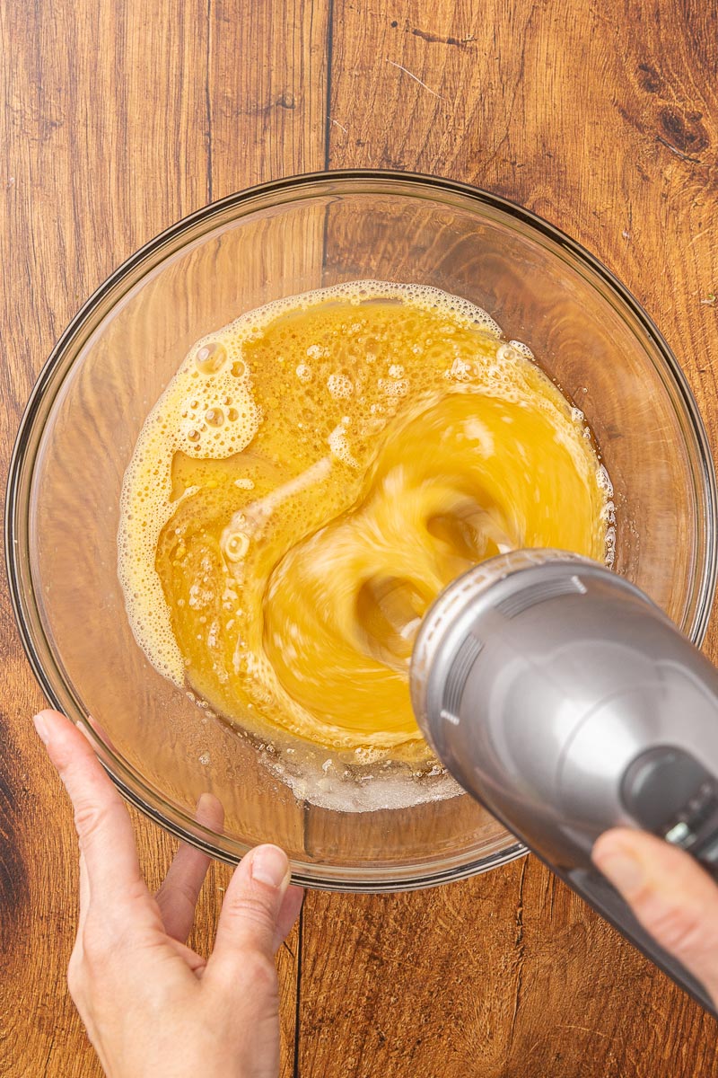 An electric mixer whisking eggs, vanilla, sugar and melted butter together.
