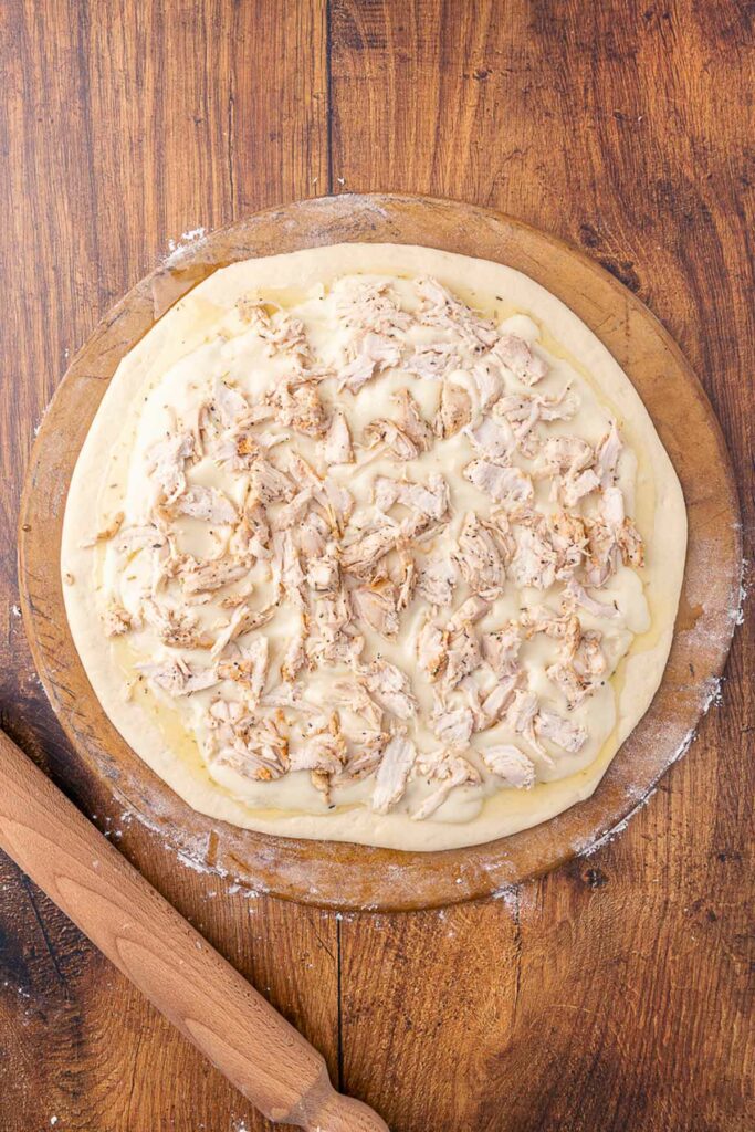 Bird's eye view of an unbaked chicken Alfredo pizza on a pizza stone ready for the oven.