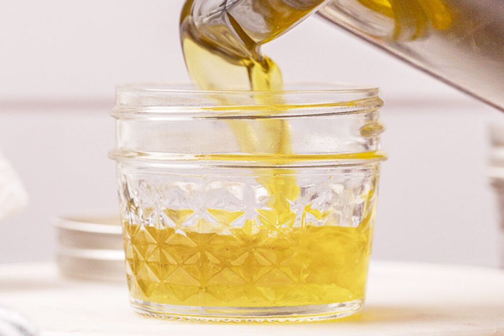 Pouring finished herbal salve from a crockpot to a glass jelly jar.