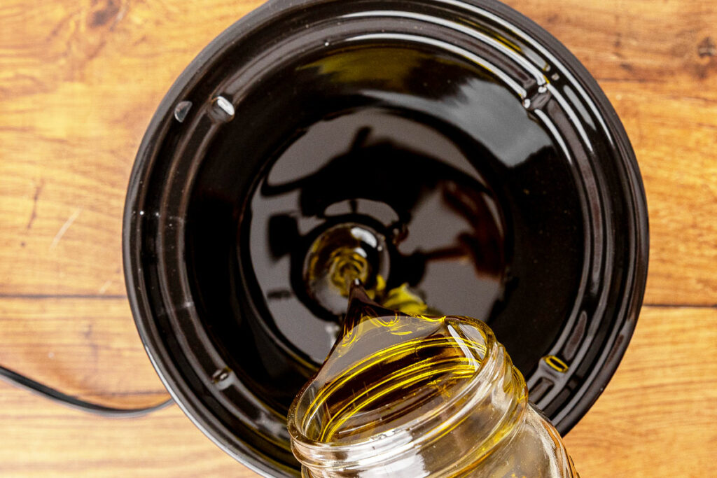 Pouring herbal infused oil into a crockpot to make an herbal salve.