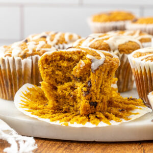 A freshly baked pumpkin chocolate chip muffin with a bite taken out of it.