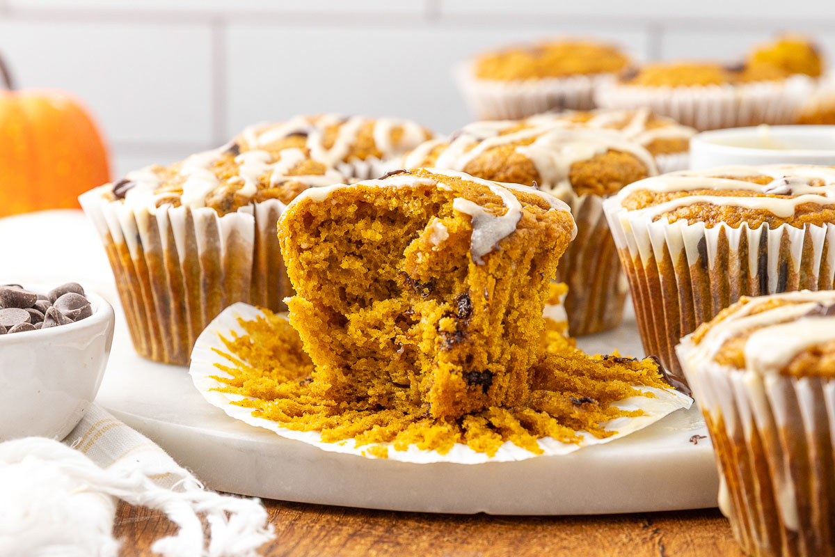A freshly baked pumpkin chocolate chip muffin with a bite taken out of it.