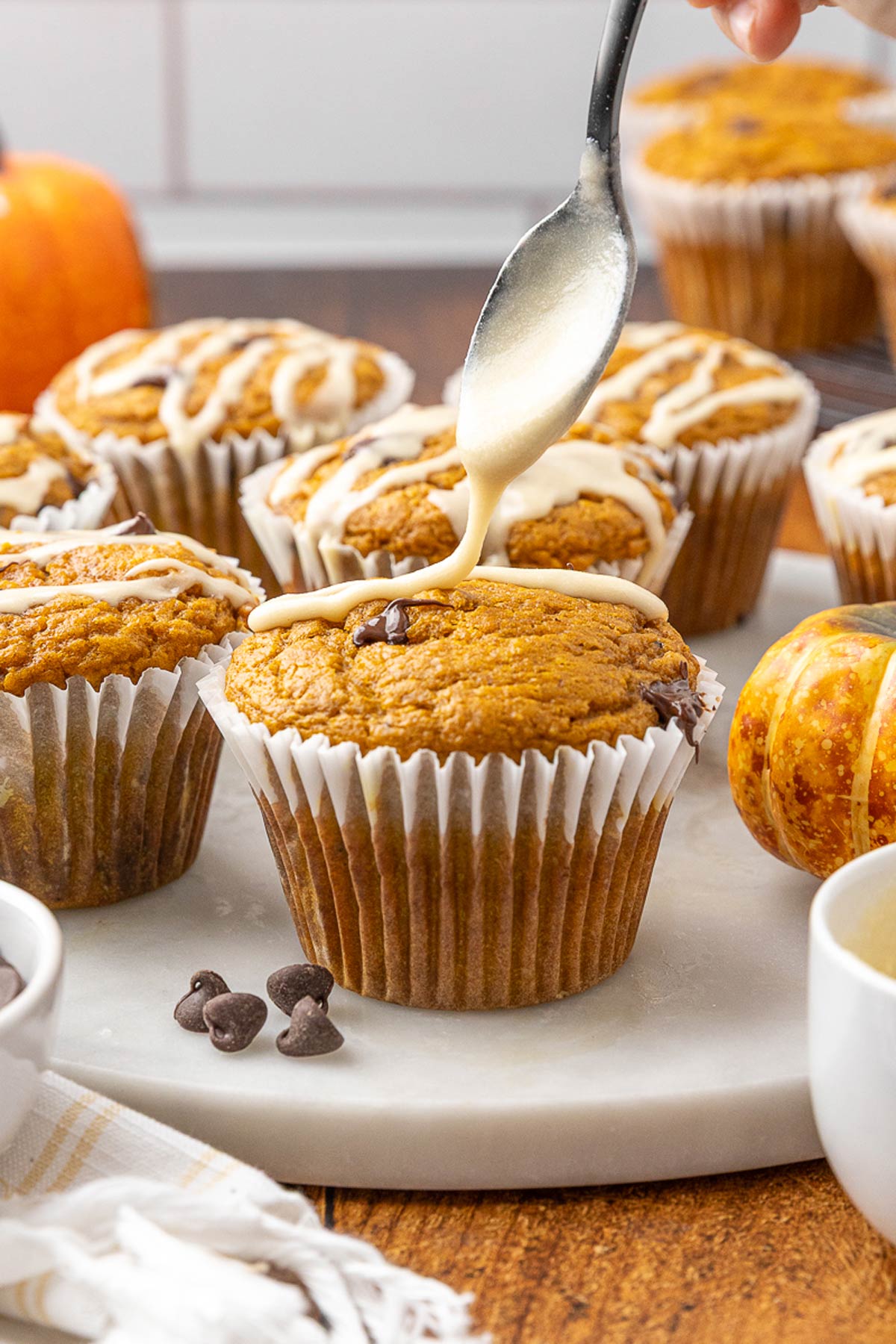 A spoon drizzling maple icing over a pumpkin chocolate chip muffin.