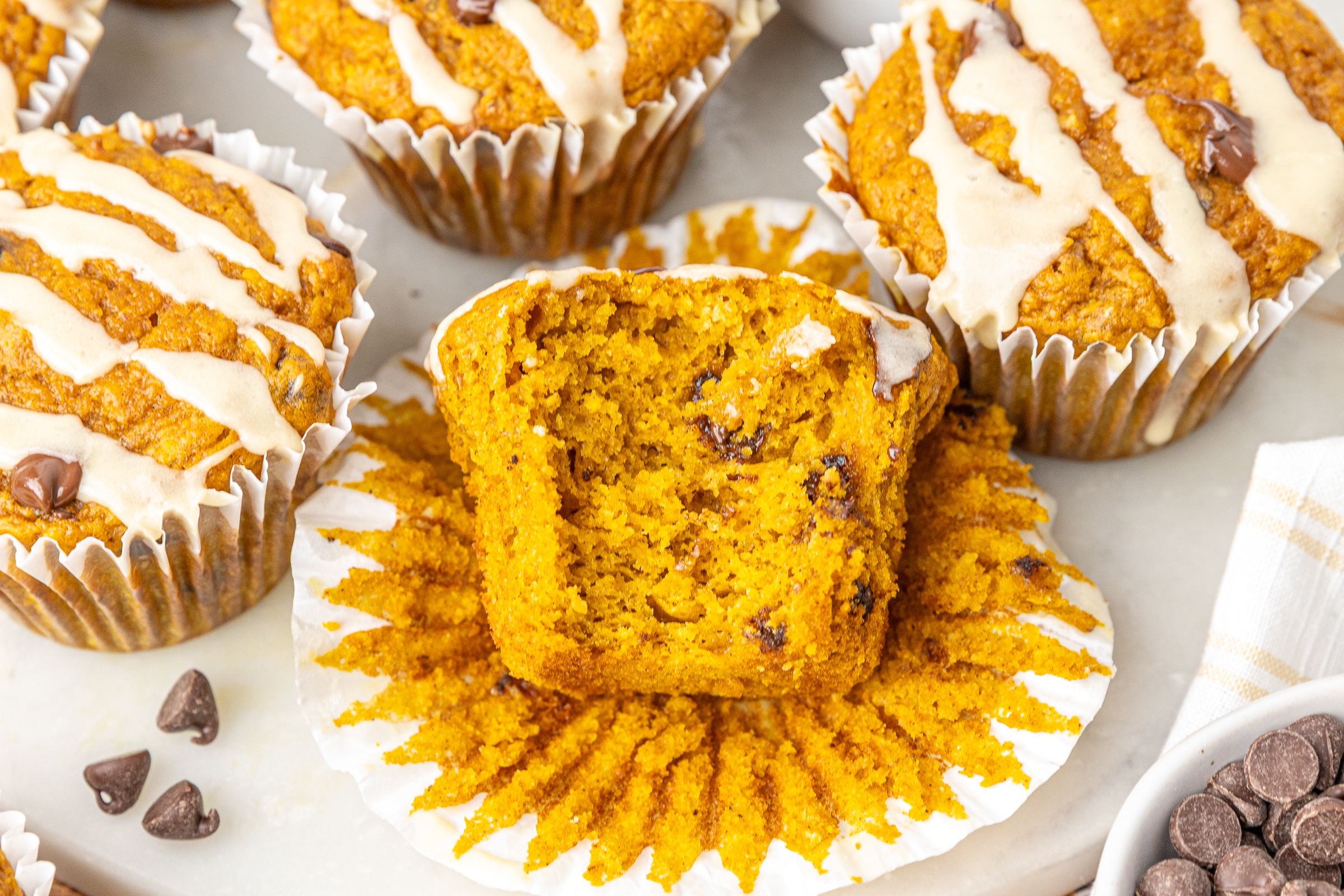 A freshly baked pumpkin chocolate chip muffin with a bite taken out of it.
