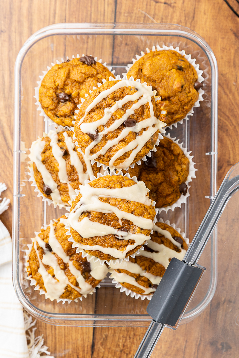 Glazed pumpkin chocolate chip muffins stacked in a storage container.