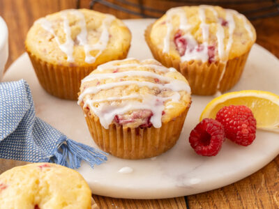 Baked raspberry cream cheese muffins sitting on a marble cutting board.