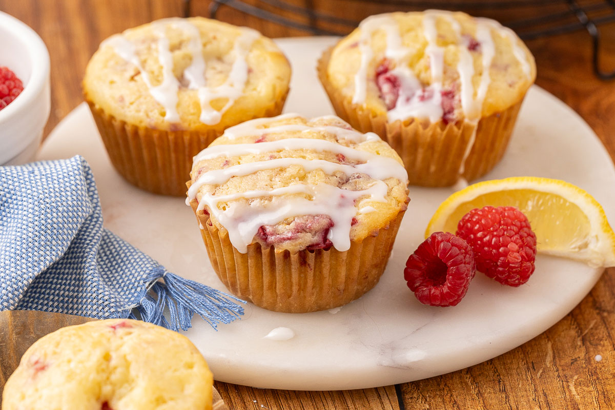 Baked raspberry cream cheese muffins sitting on a marble cutting board.
