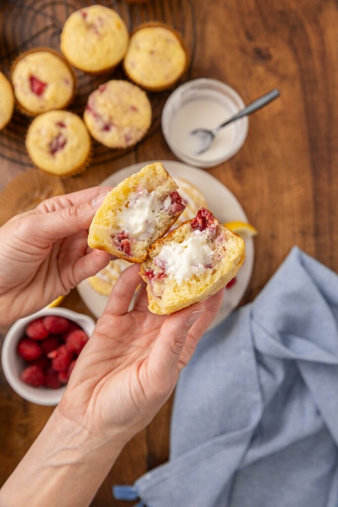 Hands holding a raspberry cream cheese muffin split in half to show the cream cheese filling.