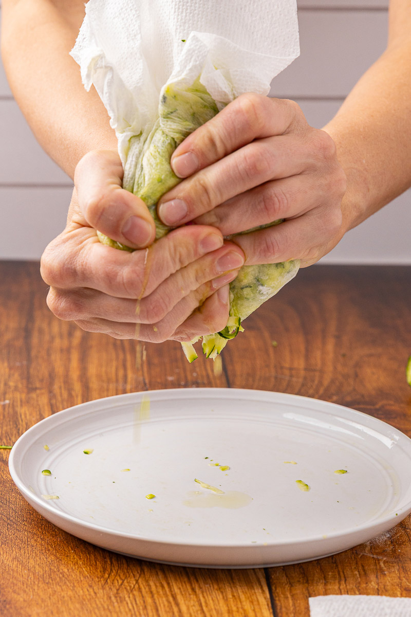Hands squeezing excess moisture from shredded zucchini.