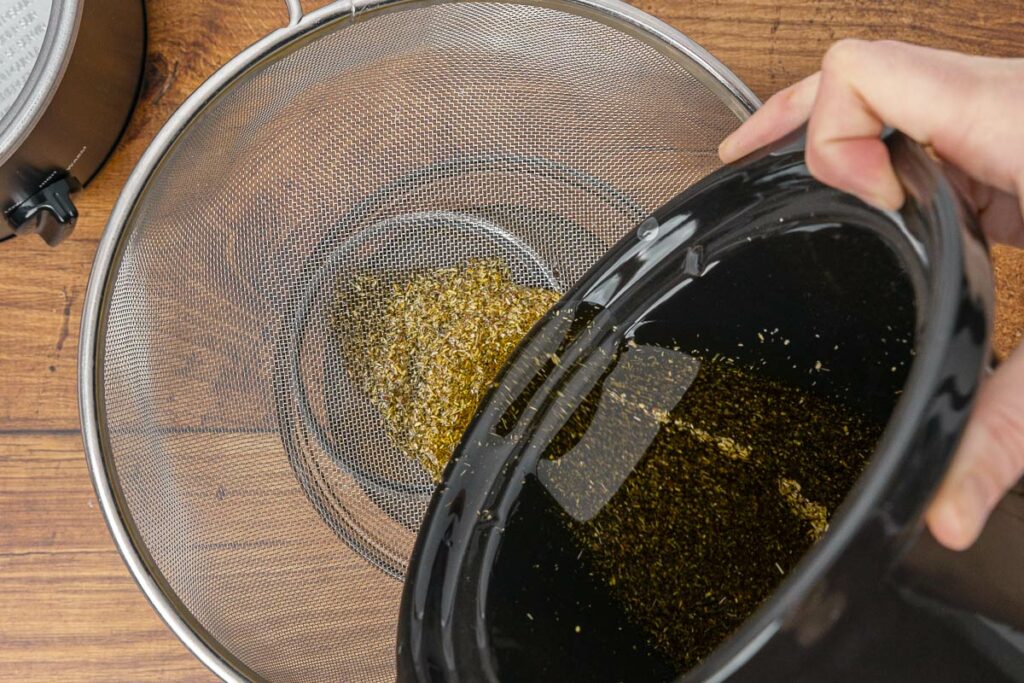 Pouring herbal infused oil through a strainer to separate the spent herbs from the oil.