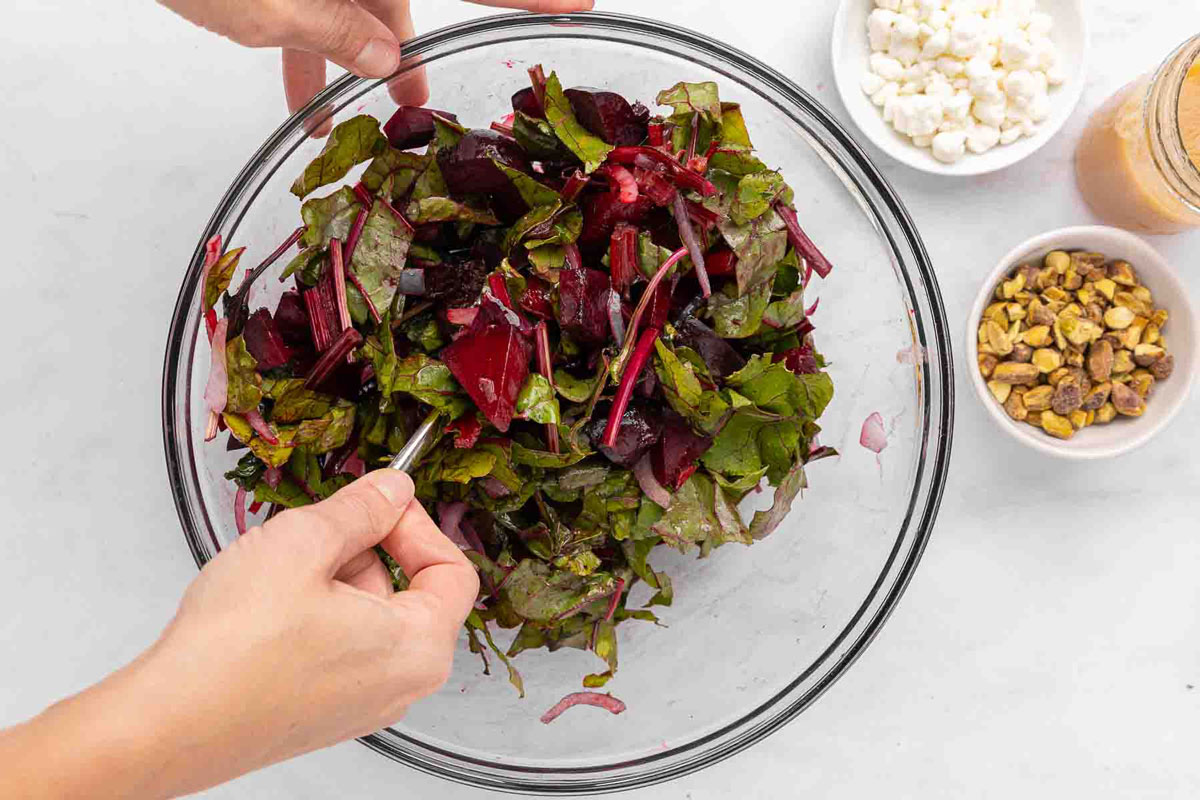 Hand holding a spoon mixing beet salad ingredients together in a mixing bowl.