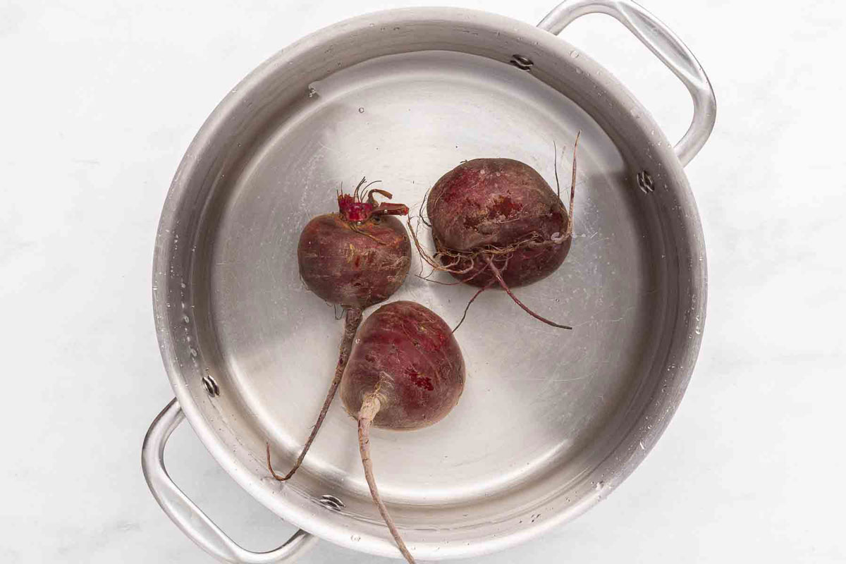 Whole beets in a saucepan of water ready to boil.