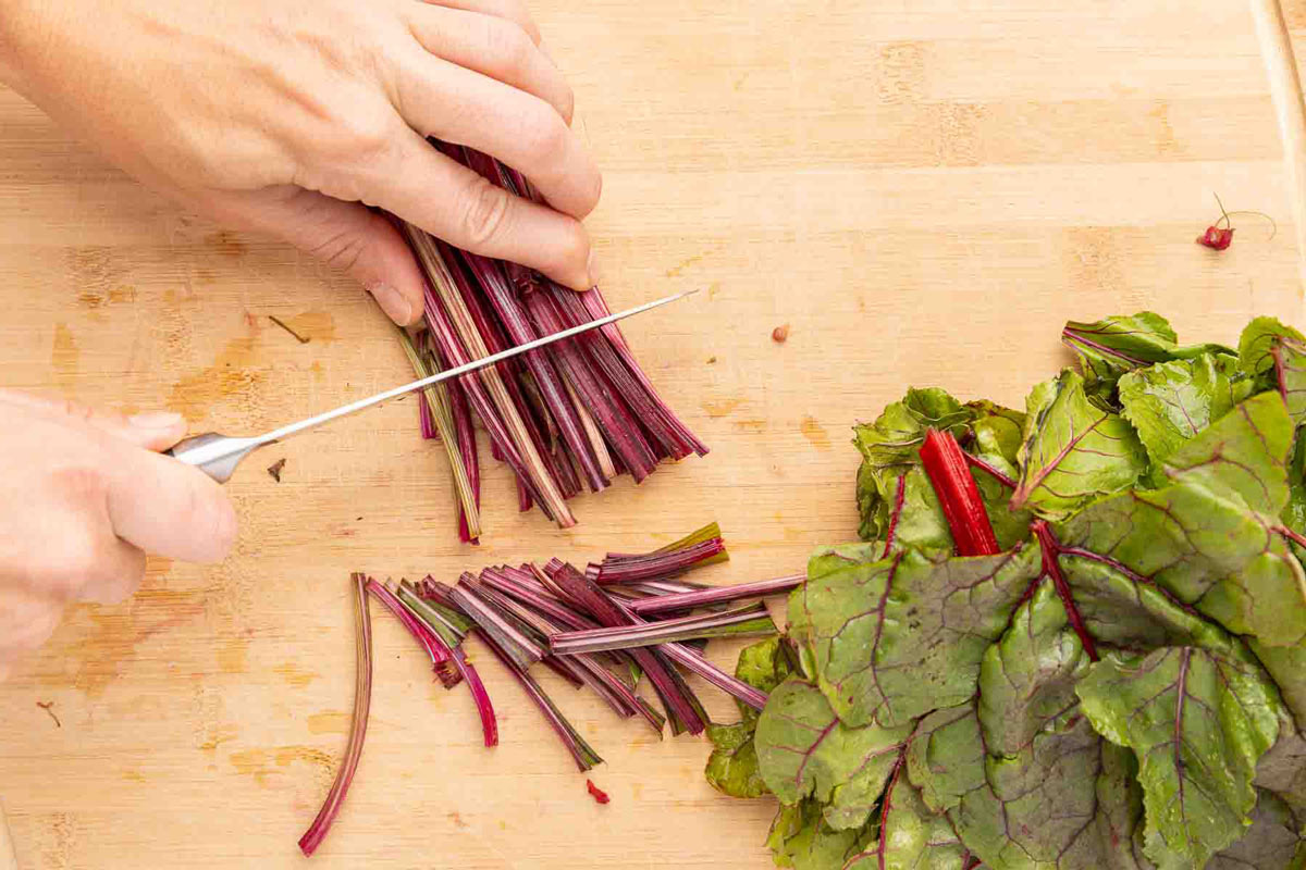 A hand holding a knife chopping beet stems into two inch pieces.