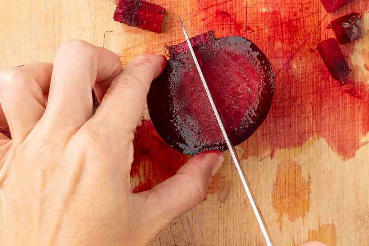 Hands holding a knife chopping boiled beets into bite sized pieces.
