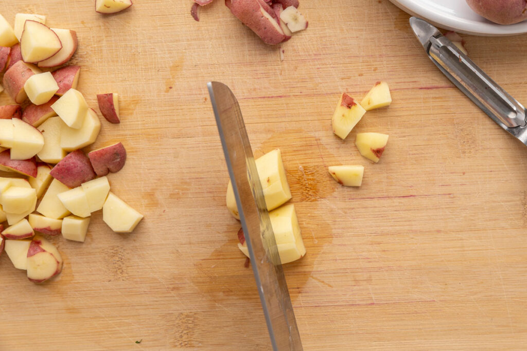 A knife chopping red potatoes on a cutting board.