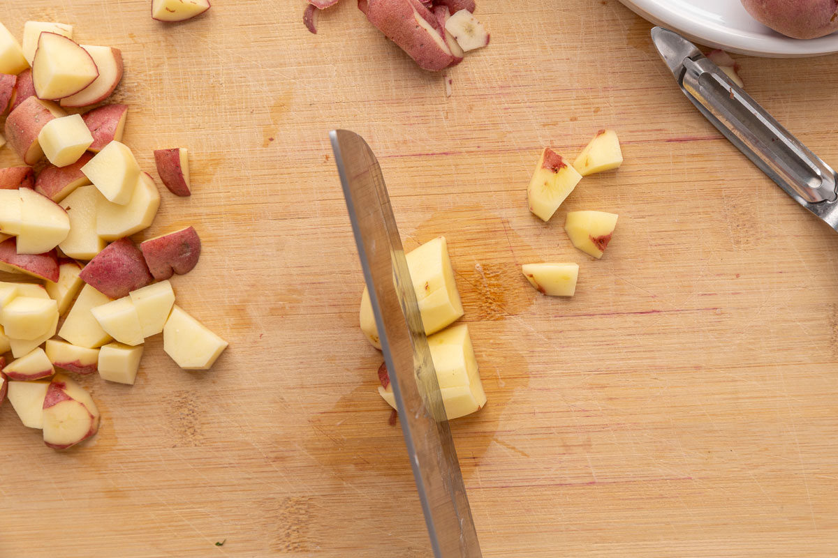 A knife chopping red potatoes on a cutting board.