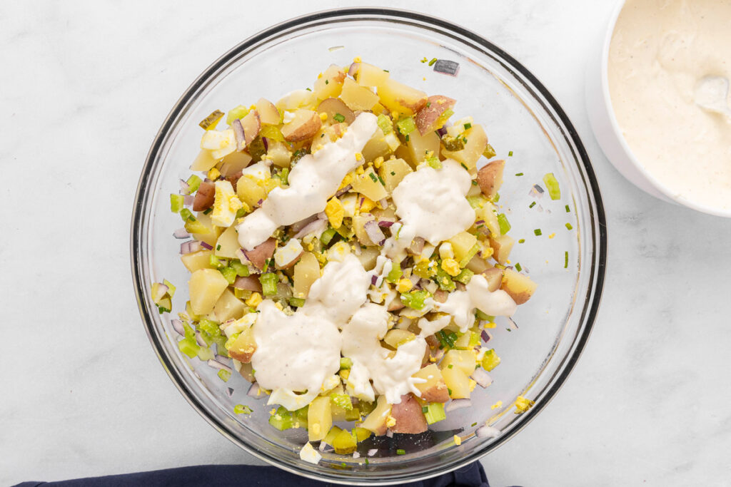 Creamy dressing drizzled over a bowl of potato salad ingredients.