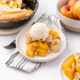 Peach cobbler served on a plate with vanilla ice cream on top.
