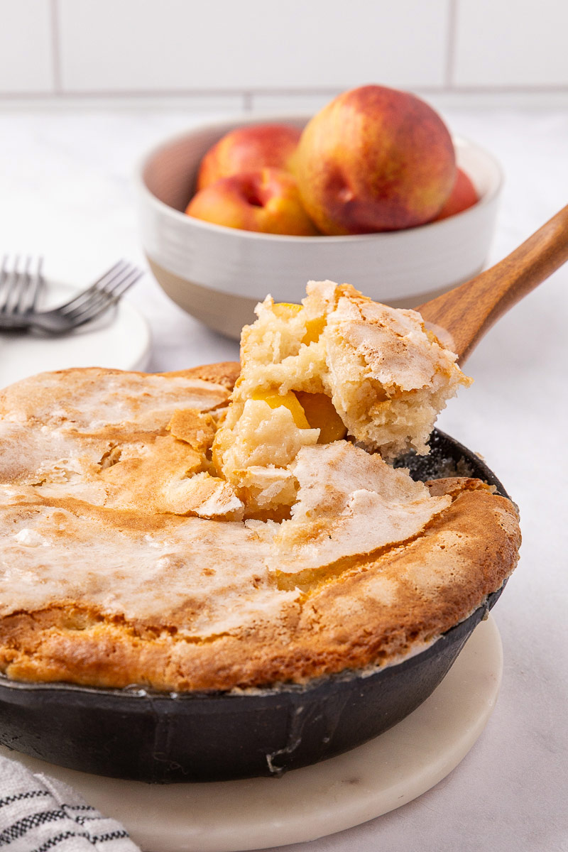 A wooden spoon scooping out peach cobbler.