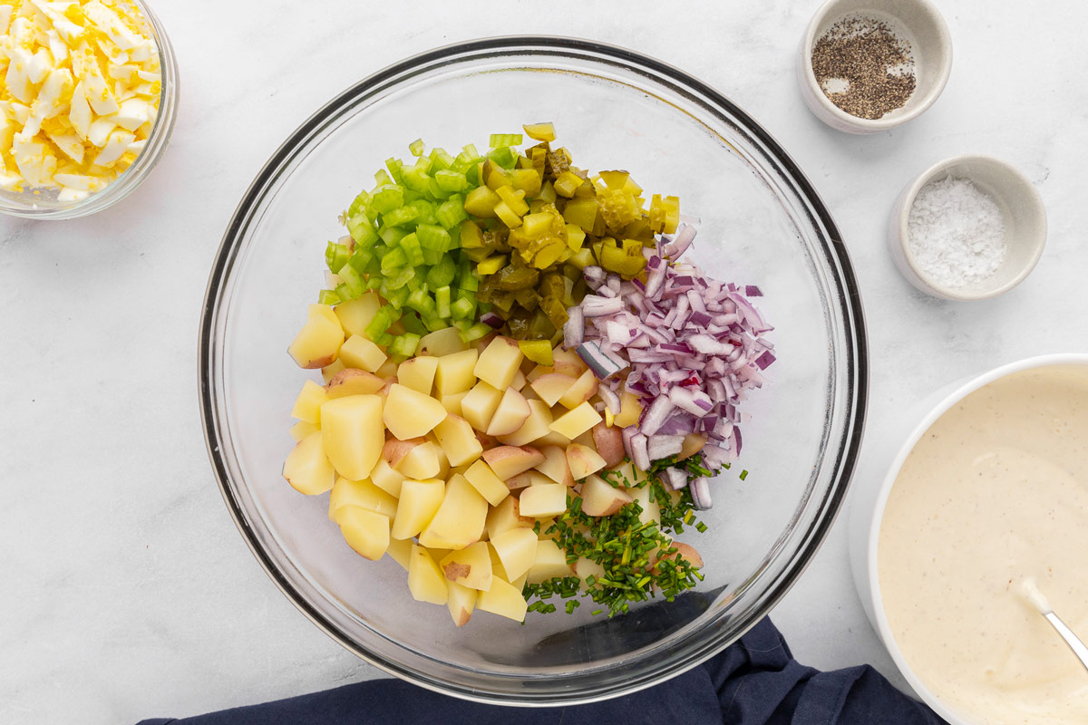 Chopped onions, celery, pickles, chives and boiled potatoes layered into a mixing bowl to make potato salad.