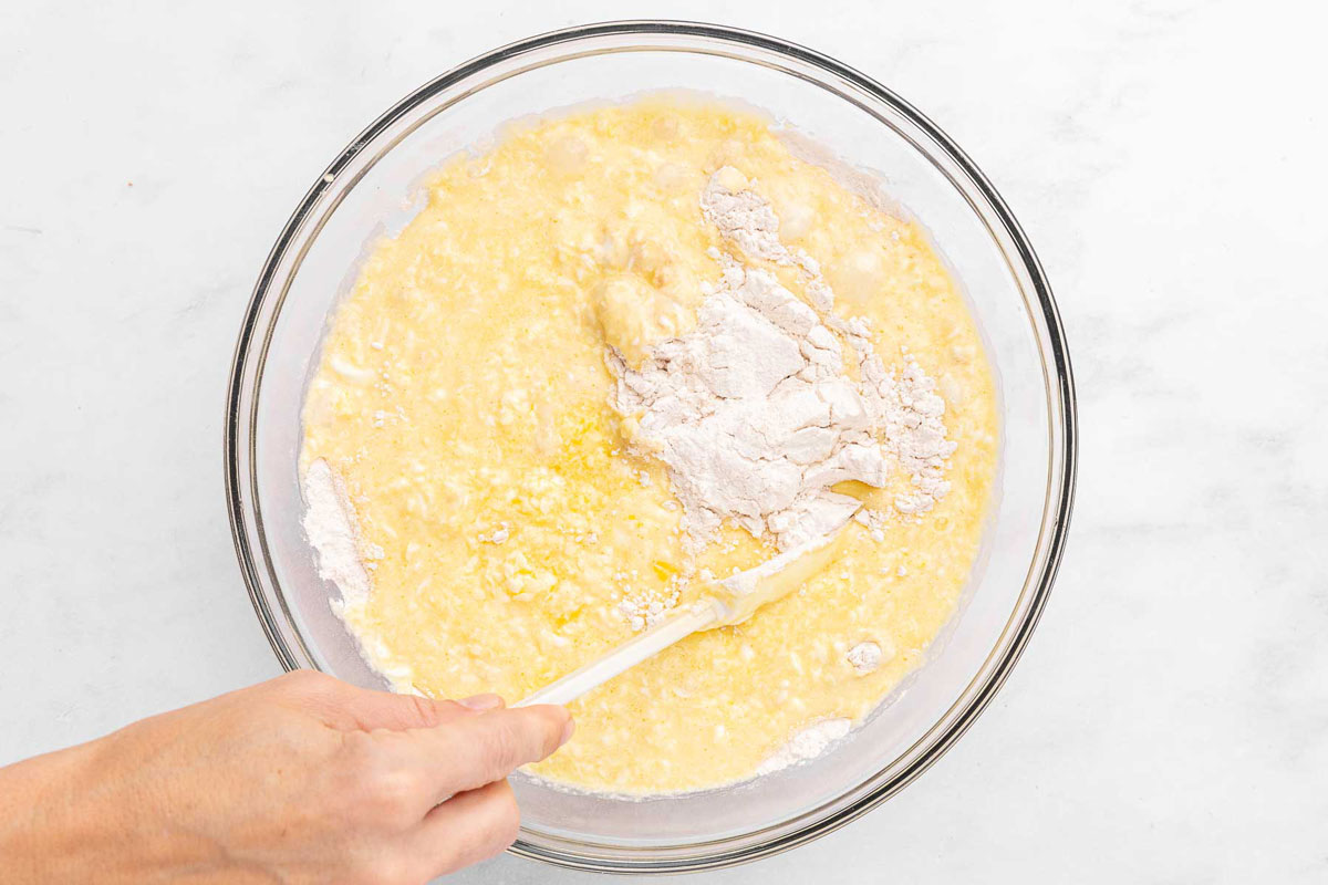 A hand holding a spatula to fold peach muffin wet and dry ingredients together.