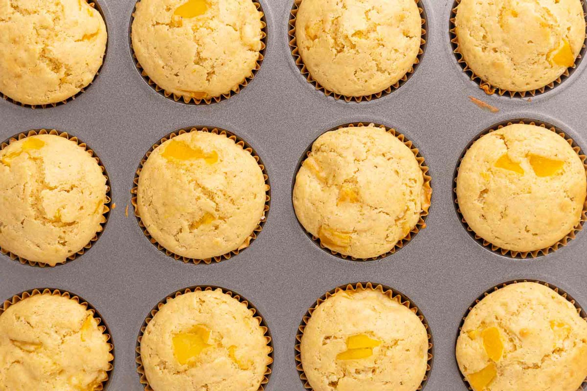 A muffin tin filled with baked peach muffins.