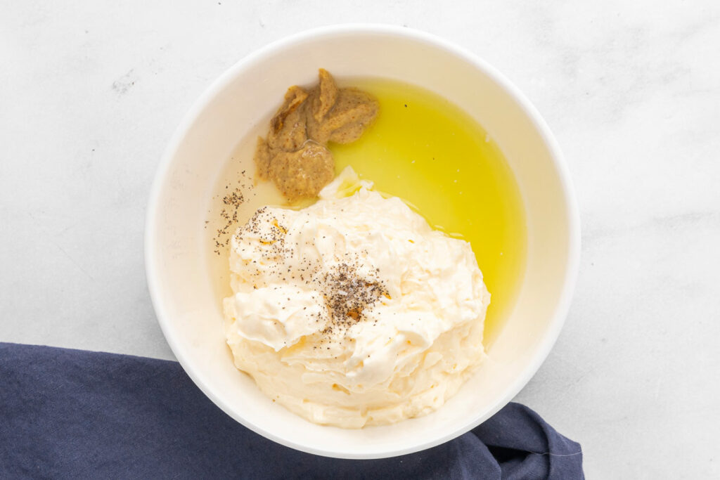 A bowl holding mayonnaise, vinegar, mustard, pickle juice, salt and pepper to mix together for a creamy dressing.