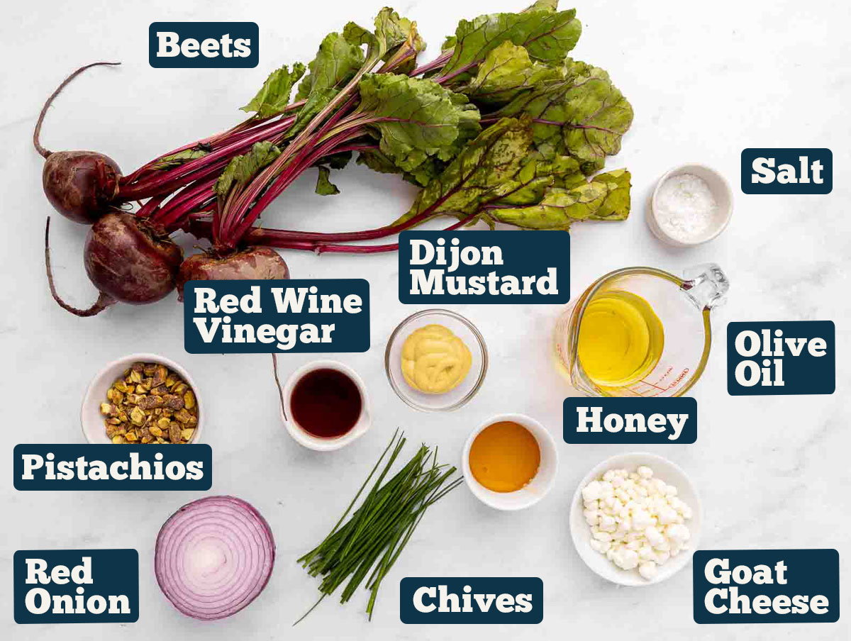 Roasted beet salad ingredients: beets with greens, onion, pistachios, goat cheese, olive oil, salt, red wine vinegar, honey, Dijon mustard, and chives.
