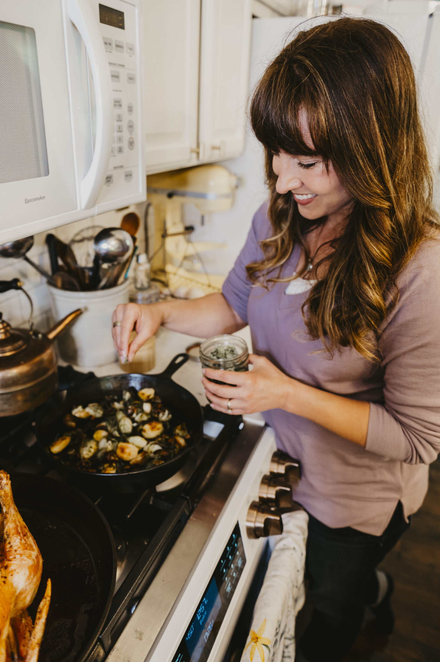 Woman smiling sprinkling salt on food in a cast iron skillet over a stove