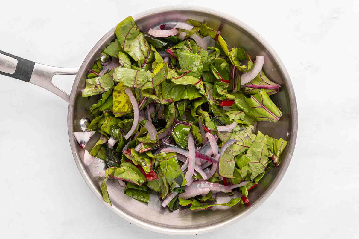 Sautéd onions and beet greens in a skillet.