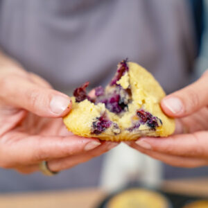 A woman splitting a blueberry muffin in half.