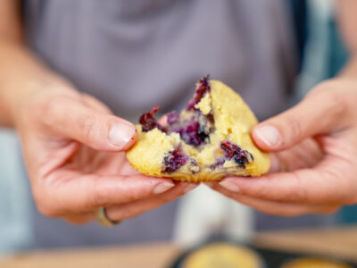 A woman splitting a blueberry muffin in half.