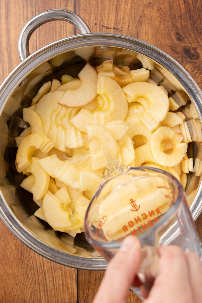 Adding water to a pot of sliced apples.