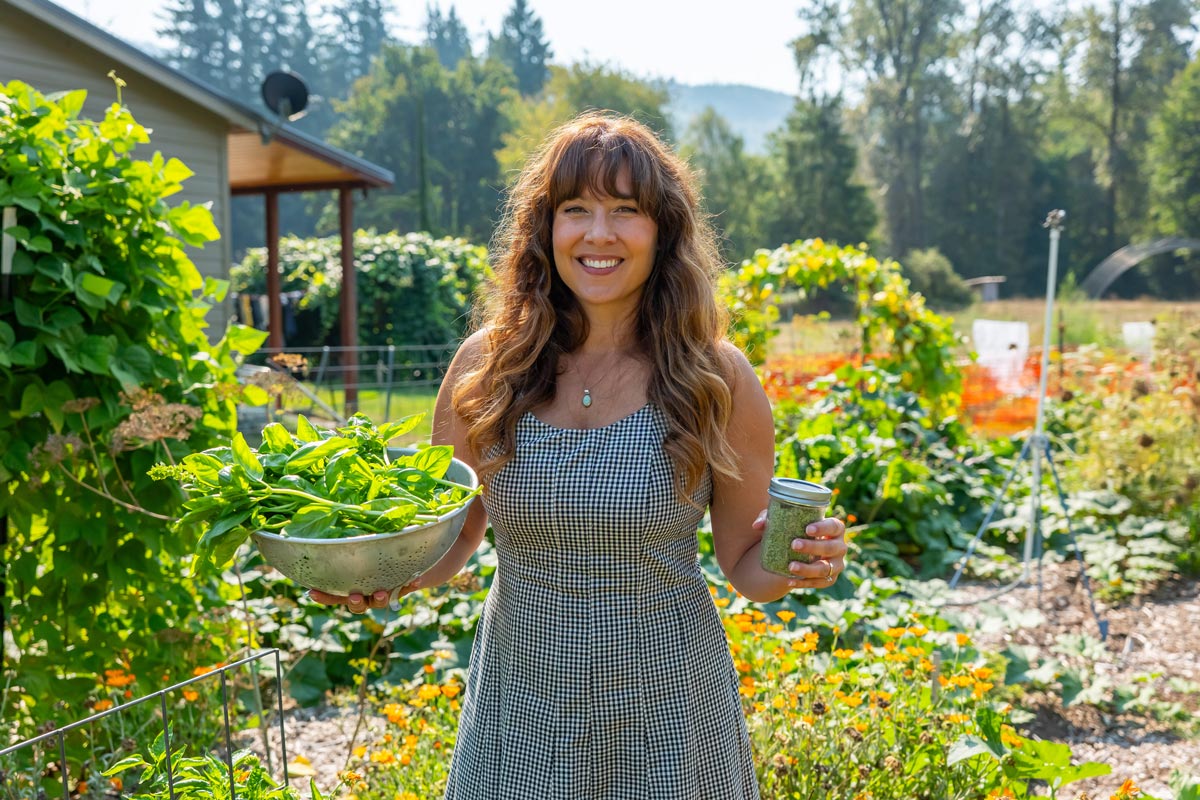 A woman holding a colander of fresh basil and a jar of basil salt.