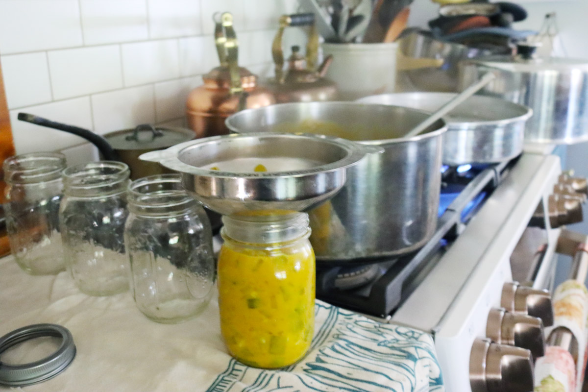 Mustard pickles being ladled into a canning jar.