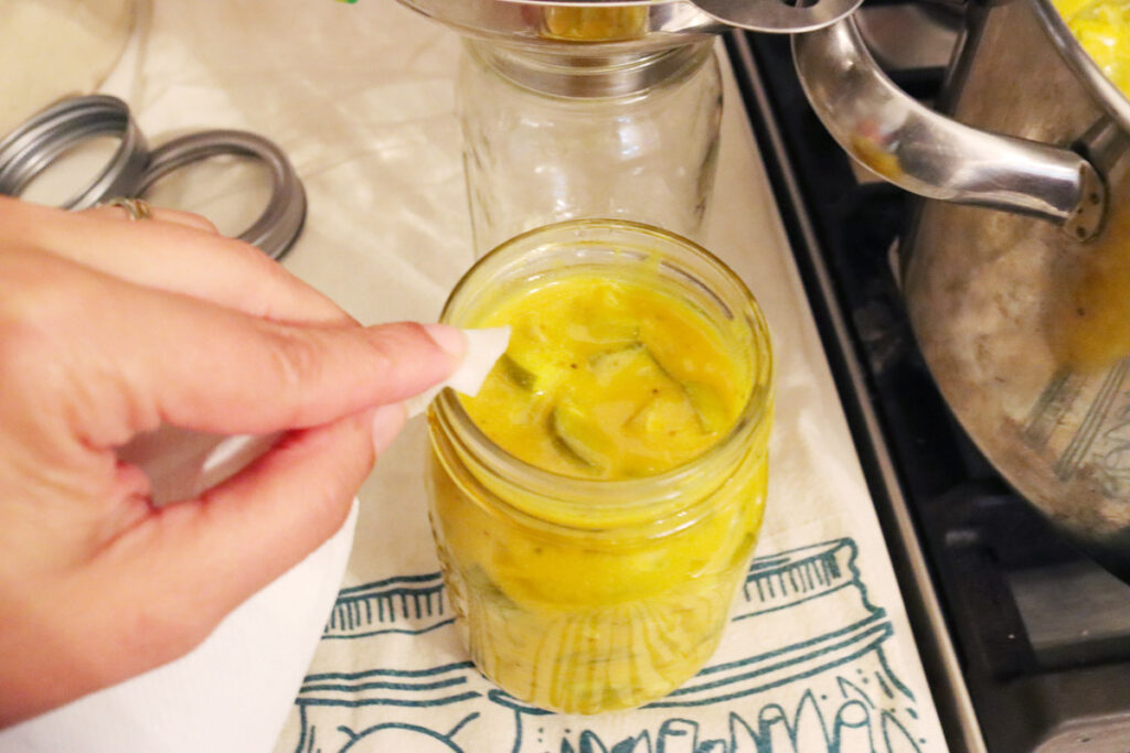 A jar of mustard pickles getting the rim wiped with a clean towel.