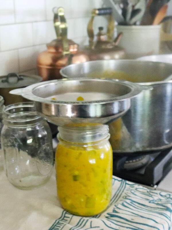 Mustard pickles being ladled into a canning jar.