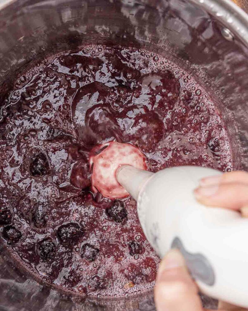 Blackberry jam being pureed with an immersion blender.