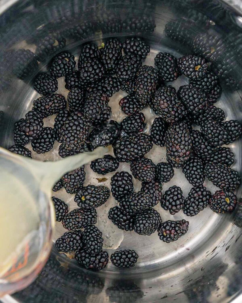 Lemon juice being added to a pot of blackberries.