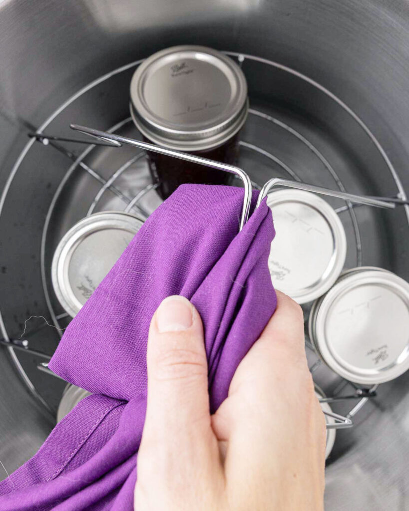 A hand lifting out jars of blackberry jam from a water bath canner.