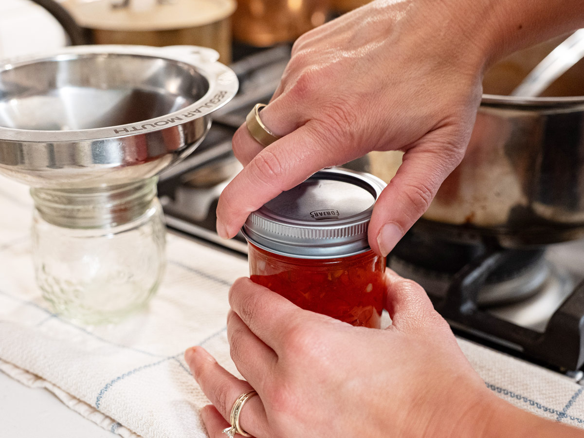 A lid being tightened on a jar of red pepper jelly.