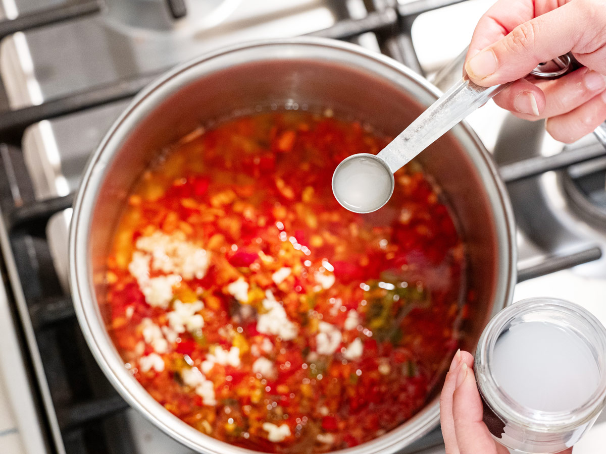 Calcium water being added to a pot of red pepper jelly.