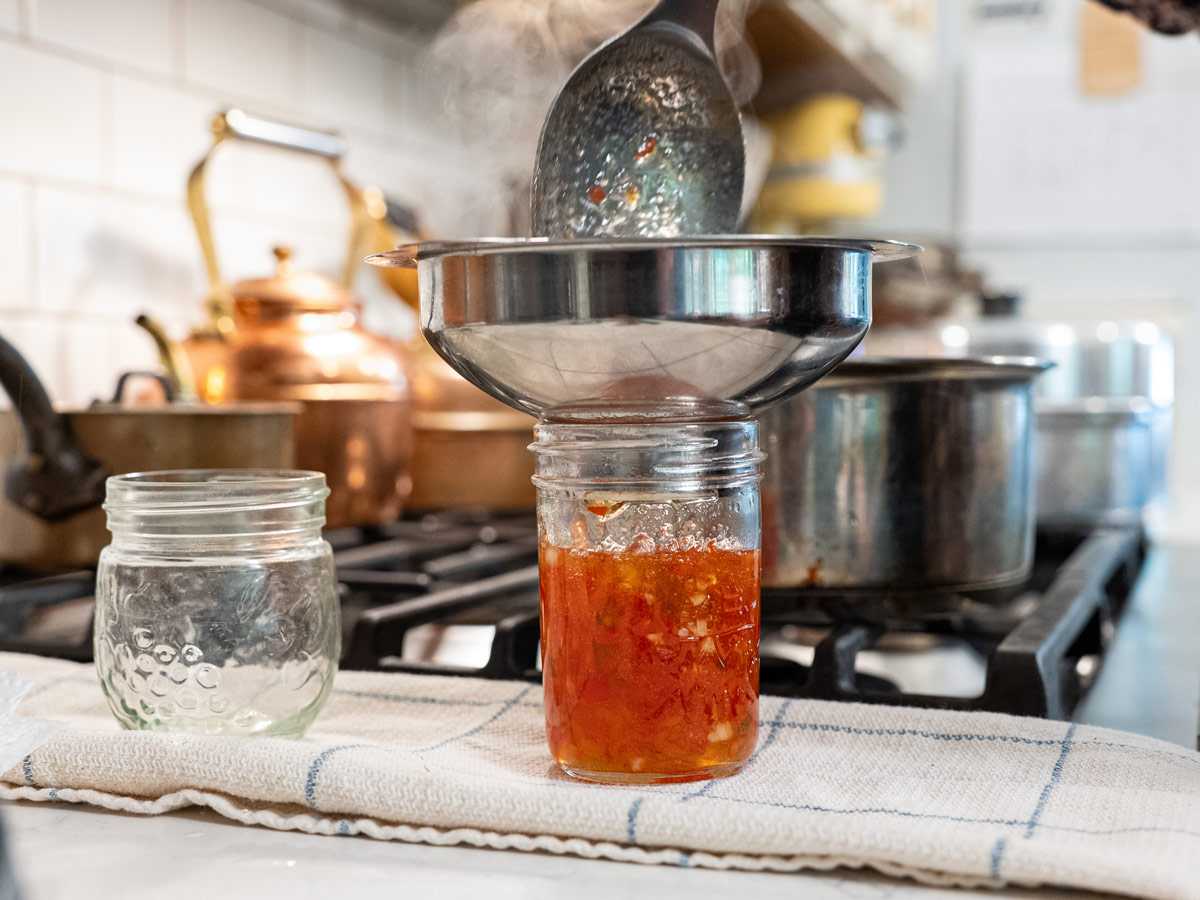 Red pepper jelly being ladled into a jar.