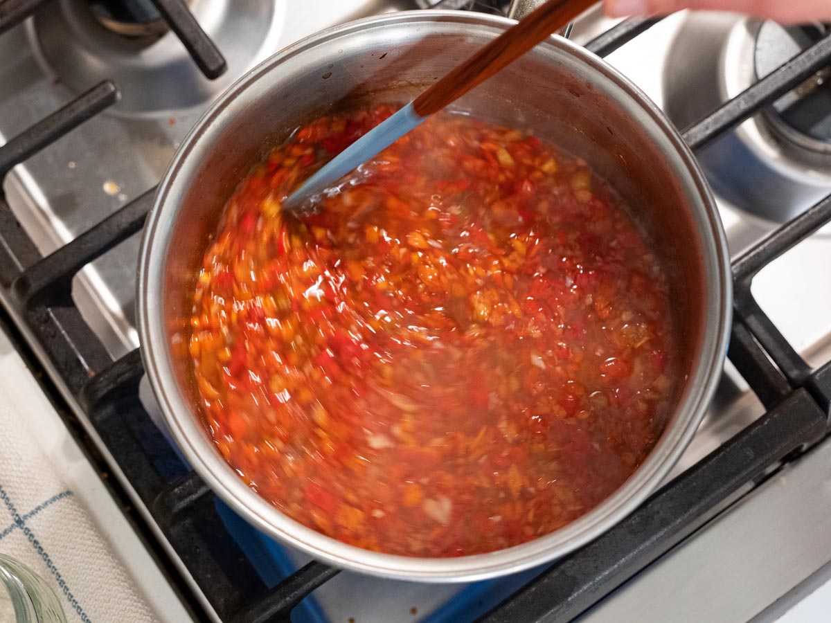 A pot of red pepper jelly being stirred.