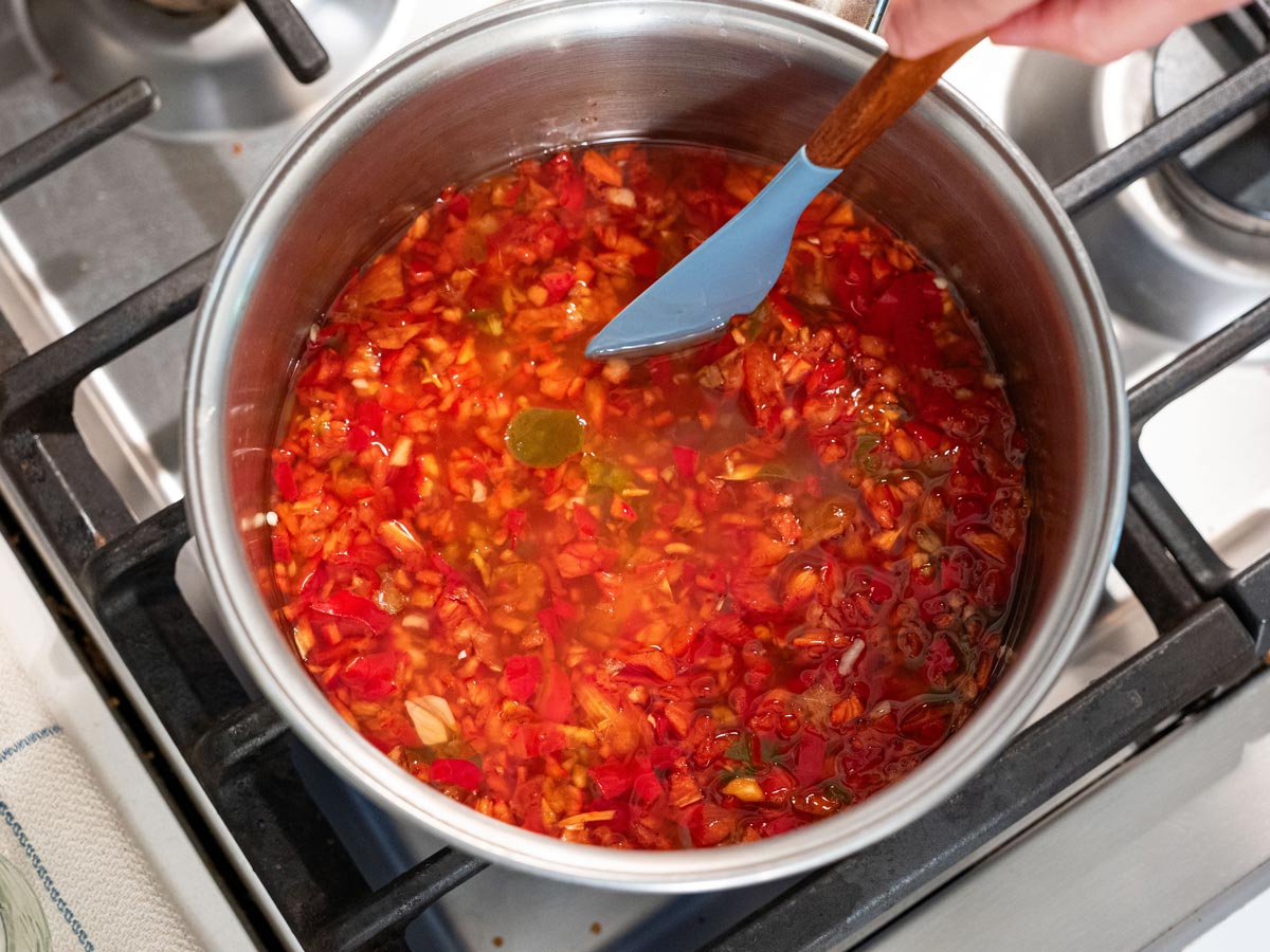 A pot of red pepper jelly being stirred.