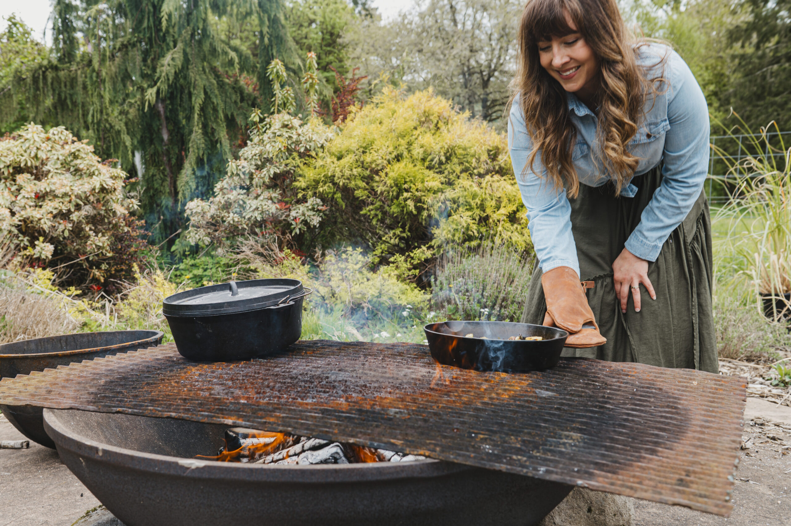 A woman cooking on an outdoor fire with cast iron.
