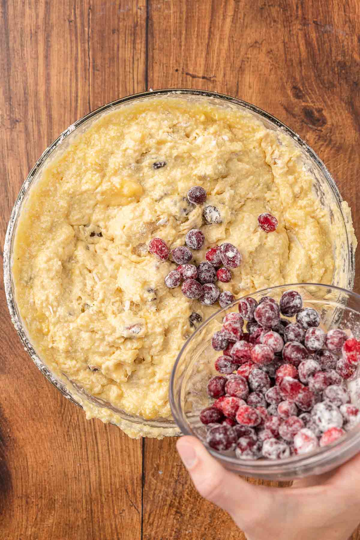 Floured cranberries being poured into muffin batter.